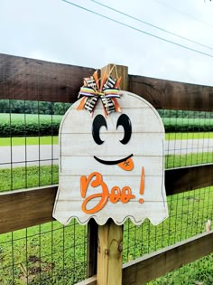 a sign that says boo on it in front of a fence with a field behind it