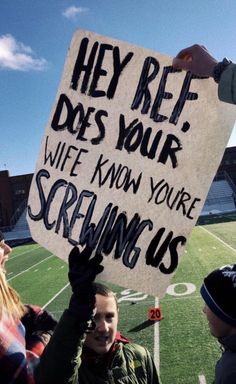 a group of people standing on top of a football field holding up a sign that reads hey ret does your wife know you're screaming us