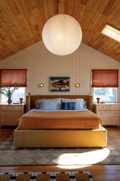 a large bed sitting under a white light in a bedroom next to a dresser and window