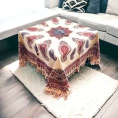 a white couch sitting next to a table covered in a blanket on top of a rug