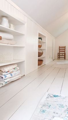 a room with white walls and wooden flooring, including shelves filled with folded towels