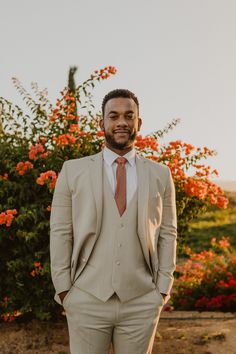 a man in a suit and tie posing for the camera with flowers in the background