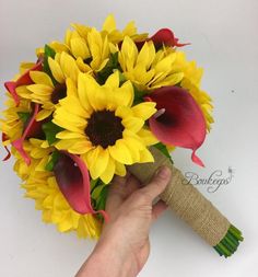 a bouquet of sunflowers is being held by a person's hand on a white surface