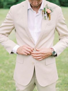 a man in a tan suit and flower boutonniere is holding his hands together