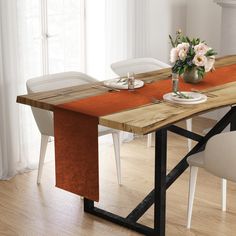 a dining table with two white chairs and an orange cloth draped over the top, in front of a window