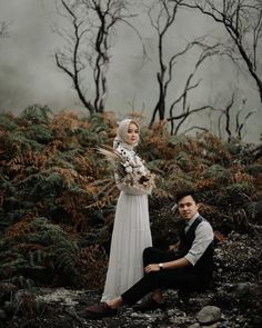 a man sitting next to a woman on top of a rocky hillside with trees in the background