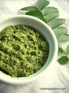 a white bowl filled with pesto next to green leaves