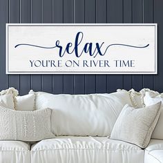 a white couch sitting next to a wooden sign that says relax you're on river time