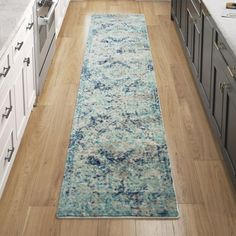 a long rug in the middle of a kitchen with white cabinets and wood flooring