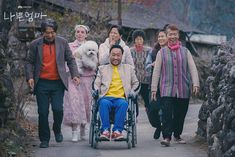 a group of people walking down a road with a man in a wheelchair behind them