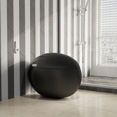 a large black ball sitting on the floor next to a window with white and gray striped walls