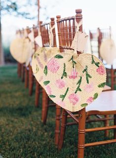 an arrangement of wooden chairs with flowers and fan shaped umbrellas on the back of them