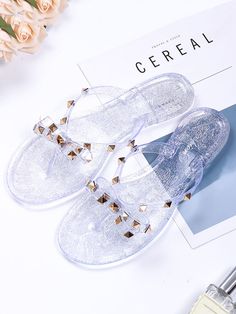 a pair of clear slippers with gold studs on the toes and bottom, next to a bottle of perfume