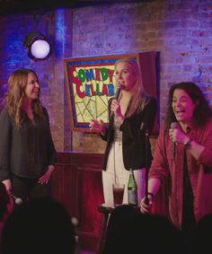 three women are standing in front of a microphone and talking to someone on the stage