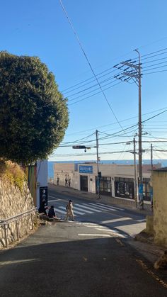 two people sitting on the side of a road next to a tree and power lines