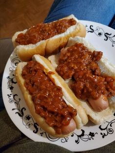 two hot dogs on buns covered in chili sitting on a black and white plate