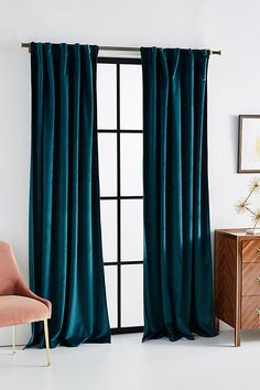 a living room with a chair and window covered in teal velvet drapes that are hanging on the wall