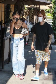 a man and woman walking down the street wearing face masks while talking on their cell phones