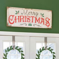 a merry christmas sign on the front door with wreaths hanging from it's sides