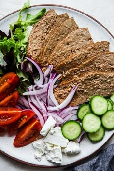 a white plate topped with meat and veggies next to cucumber slices