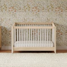 a white crib sitting in front of a wall with flowers on it