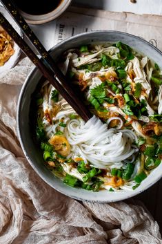 a bowl filled with noodles and vegetables next to chopsticks on top of a table