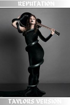 Taylor Swift wearing a long one-sleeved black body con dress holding a black guitar over her head with a long black snake wrapped around her body