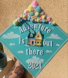 a blue graduation cap with the words adventure is out there on it and some pom - poms