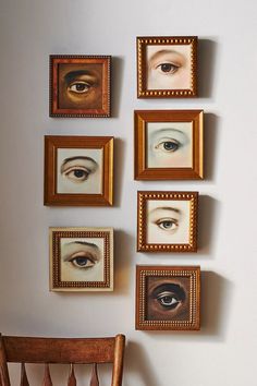 several framed pictures hang on the wall above a wooden chair with an eyeball painted on it