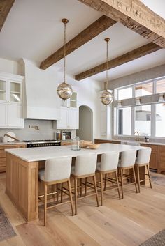 a kitchen with wooden floors and white cabinets, an island counter top and four stools