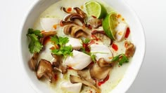 a white bowl filled with food and garnished with cilantro, mushrooms, limes