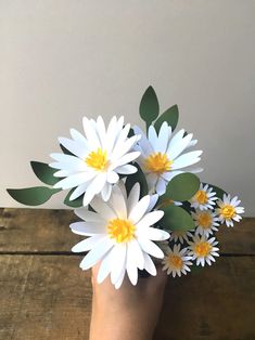 a hand holding white and yellow flowers on top of a wooden table