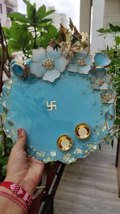 a person holding up a blue plate with flowers on it in front of some plants