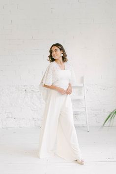 a woman standing in front of a white brick wall wearing a white top and wide legged pants