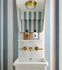 a white sink sitting under a mirror next to a gold faucet in a bathroom