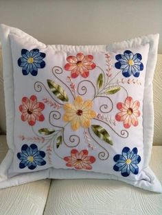 a white pillow with blue, red and yellow flowers embroidered on it's side