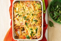 a casserole dish with pasta and vegetables in it on a red napkin next to a green salad