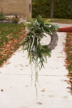 a person is holding a wreath with greenery on it and walking down the sidewalk