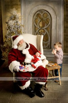 a little boy standing next to santa clause sitting in a chair