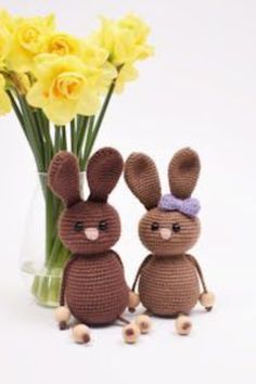 two crocheted bunnies sitting next to each other in front of a vase with yellow flowers