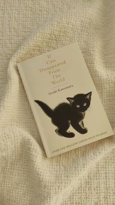 a book with a black cat on it laying on a white cloth covered bed sheet