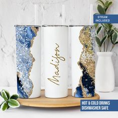 three personalized tumbles with gold and blue glitter on them, sitting on a wooden tray