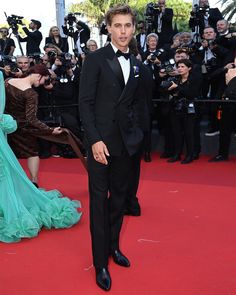 a man in a tuxedo and bow tie standing on a red carpet next to photographers