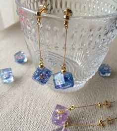 some blue and purple glass cubes sitting on a table next to gold ear pins