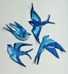 three blue birds flying next to each other on a white surface with one bird in the air