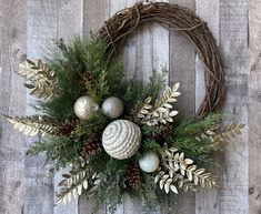 a wreath with pine cones, balls and greenery on a wooden background that is hung on the wall