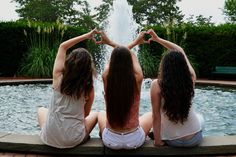 three young women sitting on the edge of a fountain making heart shapes with their hands