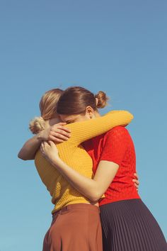 two young women hugging each other in front of a blue sky with no clouds on it