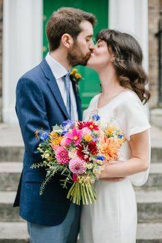 a bride and groom kissing in front of a green door with flowers on the bouquet