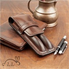 a leather wallet and pen holder on a wooden table next to a silver teapot